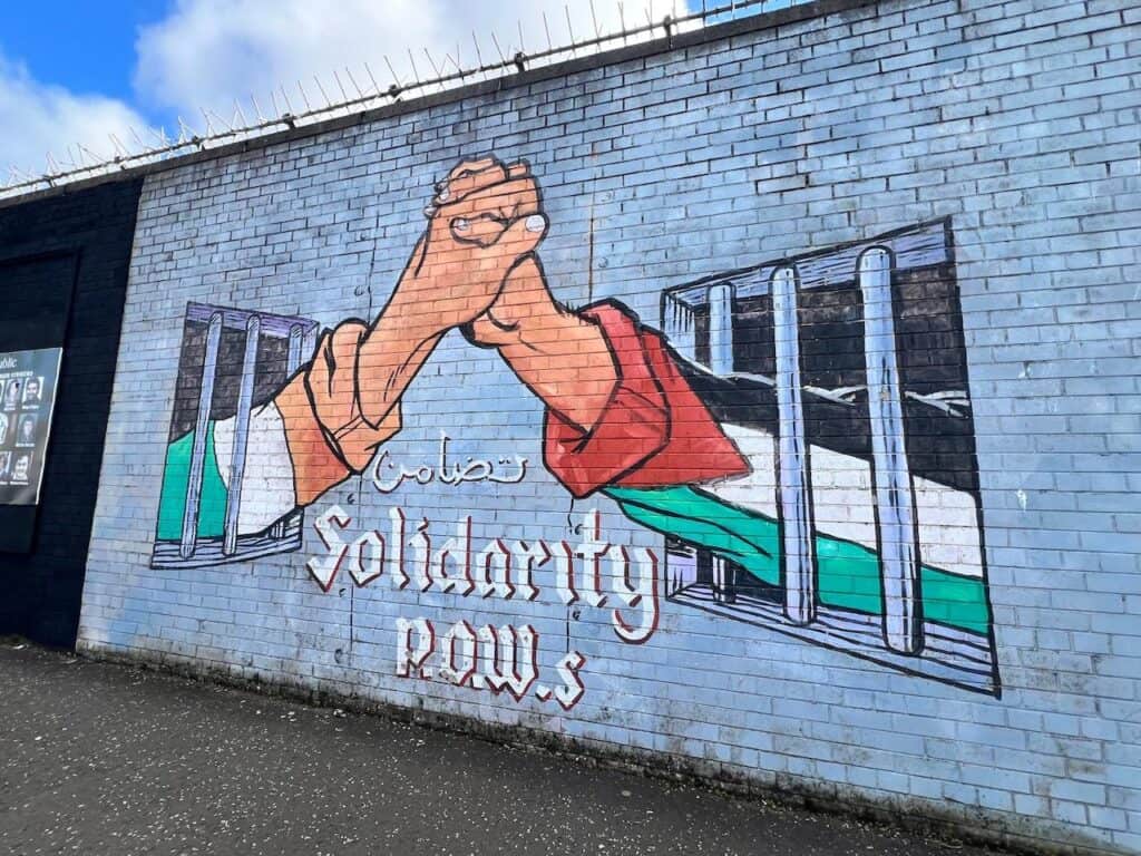 Belfast mural showing hands joined across barriers with the words solidarity knows no borders